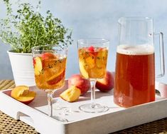 two glasses of apple cider on a tray next to some sliced peaches and apples