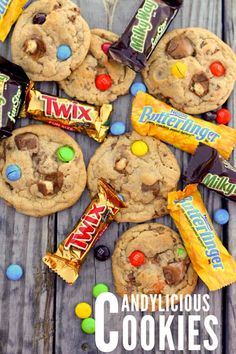 chocolate chip cookies with m & m candies and candy bars on top, sitting on a wooden table