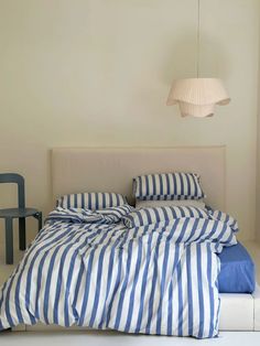 a bed with blue and white striped comforter next to a lamp on the wall