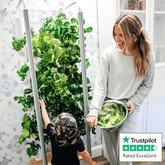 a woman holding a bowl with lettuce in it and a child reaching up to pick something out of the plant