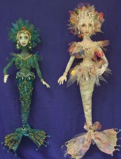 two mermaid dolls sitting next to each other on a blue background, one in green and the other in gold