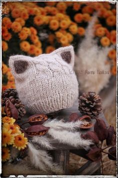 a knitted cat sitting on top of a wooden chair surrounded by flowers and leaves