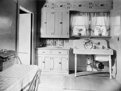 an old photo of a kitchen with sink, cabinets and table in the middle of it