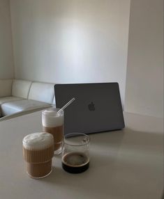 an apple laptop computer sitting on top of a white table next to two cups of coffee