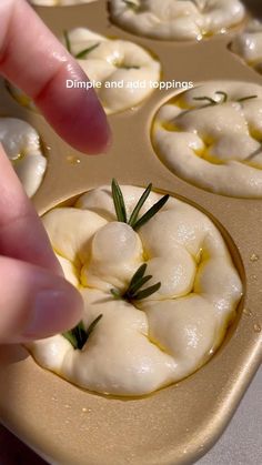 a person placing some food in a muffin tin with olives on top and rosemary sprigs sticking out of it