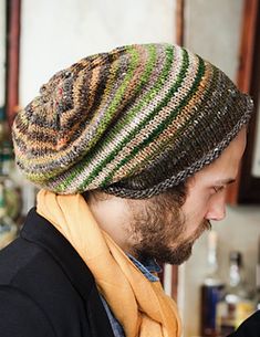 a man with a beard wearing a knitted hat and scarf in front of a bar