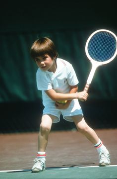 a young boy holding a tennis racquet on top of a tennis court