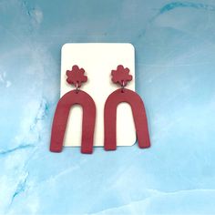 red wooden earrings with flowers on them are sitting on a white plate against a blue background