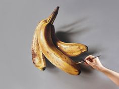 a person holding a pen in front of three bananas on a gray surface with shadow coming from them