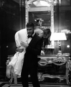 a man in a tuxedo is hugging a woman's head while standing next to a mirror