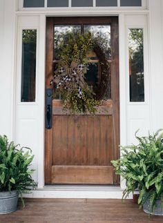 a wreath on the front door of a house with two potted plants next to it