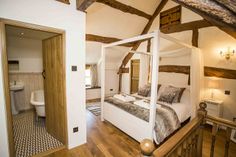 a white bed sitting inside of a bedroom on top of a wooden floor next to a bathroom