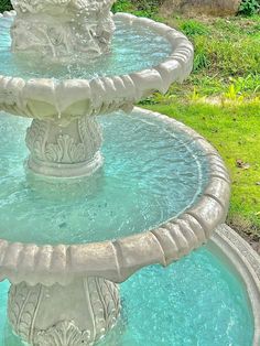 a water fountain in the middle of a grassy area with trees and bushes behind it