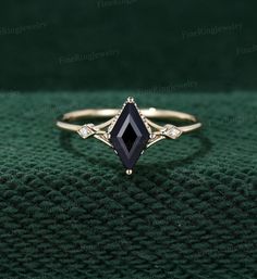 an elegant black diamond ring with diamonds on the sides, sitting on a green cloth