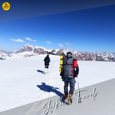 two skiers walking up the side of a snow covered slope with mountains in the background