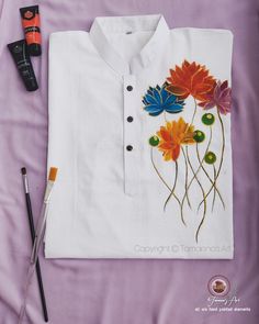 a white shirt with flowers painted on it and some paintbrushes next to it