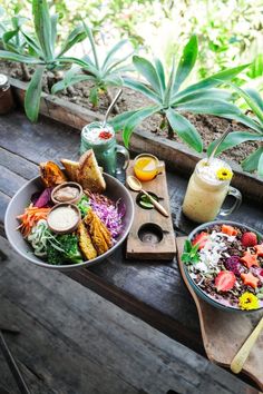 two plates of food sit on a wooden table next to some plants and flowers in the background