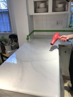 a person using a hair dryer on top of a white counter in a kitchen