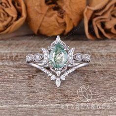 an engagement ring with a green stone surrounded by white diamonds on top of a wooden table