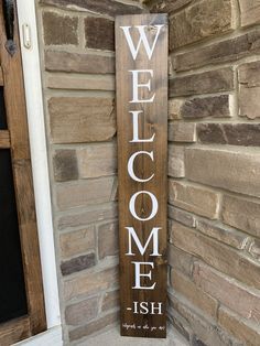 a wooden welcome sign sitting on the side of a brick wall next to a door