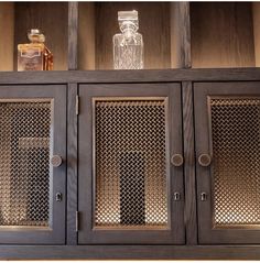 an empty glass bottle is sitting on top of a wooden cabinet with metal mesh doors