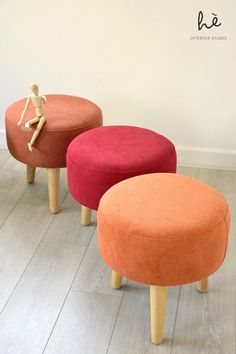 three small stools with wooden legs in various colors and sizes, sitting on a hard wood floor