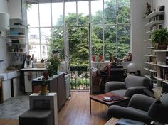 a living room filled with furniture next to a window covered in lots of books and plants