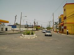 cars are driving down an empty street in front of yellow buildings and palm trees on the other side