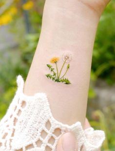 a woman's wrist with a small flower tattoo on the left side of her arm