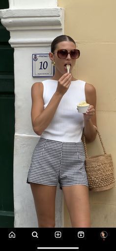 a woman in shorts is eating something while standing next to a wall with a sign on it