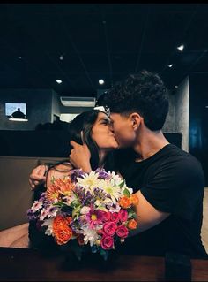 a man kissing a woman on the cheek and holding a bouquet of flowers in front of her