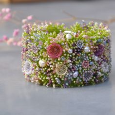 a close up of a bracelet made out of beads and flowers on a table next to a plant