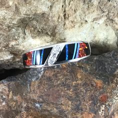 This beautiful Sterling Silver Ring, as part of the Red Moon Collection, features Black Jade, Kingman Turquoise and Blue, Green & Red Lab Opal. with a cascade of three small Cubic Zirconia in the center. Ring Width: 5/16" The ring is designed by David Rosales, one of the finest contemporary Southwest Artists in the world. He is the founder and co-owner of Supersmiths, Inc. of Gallup, NM. Each ring is custom made and carries a lifetime guarantee. Red Inlay Ring, Red Ring With Inlay, Red Inlay Ring Jewelry, Red Multi-stone Diamond Jewelry, Red Sterling Silver Rings With Inlay, Red Sterling Silver Ring With Inlay, Red Sterling Silver Jewelry With Inlay, Unique Red Diamond Jewelry, Red Inlay Rings For Gifts