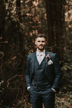 a man wearing a suit and tie standing in the woods