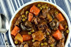 a bowl filled with meat and vegetables on top of a blue table cloth next to a spoon