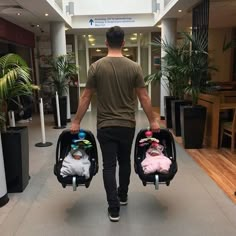 a man carrying two baby strollers down a hallway