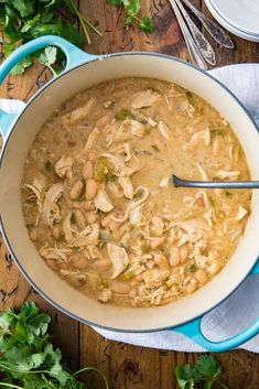 a bowl of chicken and bean soup on a wooden table with parsley next to it