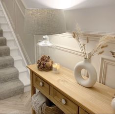 a table with a lamp and vase on it next to some stairs in a house