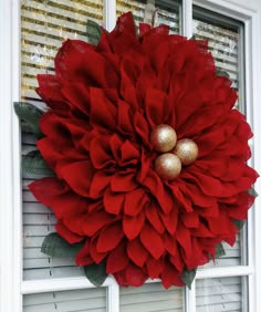 a large red flower hanging on the side of a window with gold balls in it