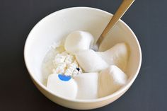 a white bowl filled with marshmallows and powdered sugar next to a spoon