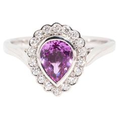 Sweetly crafted in 18 carat white gold, The Priya Ring is a delight. Her pear shaped pink purple sapphire is set in a halo of diamond embellished lace. A loving way to ask to share a life with your beloved, she is the perfect mix of romance and glamour. The Priya Ring Gem Details  The centre pear shaped purplish pink sapphire measures 7.20x5.50x3.85 millimetres and is estimated to weigh 1.10 carats. The sapphire is lightly included and shows very slight signs of wear. The eighteen round brillian Elegant Pink Sapphire Jewelry With Halo Design, Elegant Pink Sapphire Halo Jewelry, Elegant White Gold Ring With Pink Sapphire, Elegant White Gold Pink Sapphire Rings, Elegant White Gold Rings With Pink Sapphire, Pink Pear-shaped Gemstone Rings, Purple Pink Sapphire Ring With Center Stone, Fine Jewelry Pink Sapphire Ring In Purple, Pink Sapphire Ring In White Gold With Halo Setting