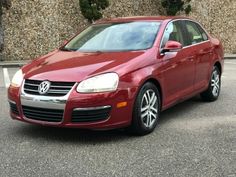 a red car is parked in front of a stone wall and some bushes on the side of the road