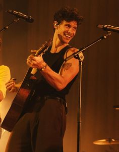 a man holding a guitar while standing next to another man with microphones behind him