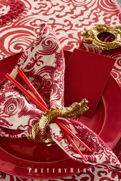 red and white place setting with napkins and gold decorations on the table top,