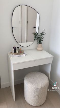 a white dressing table with a mirror and stool in front of it, next to a potted plant