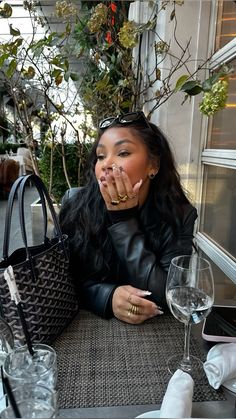 a woman sitting at a table with her hand on her mouth and holding a purse in front of her face