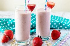 two glasses filled with smoothie and strawberries on top of a blue tablecloth