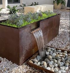 a water feature in the middle of a garden with rocks and gravel around it, next to a building