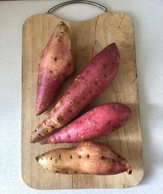 three sweet potatoes are on a cutting board