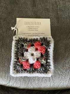 a crocheted square with red and white flowers on it sitting on top of a gray blanket